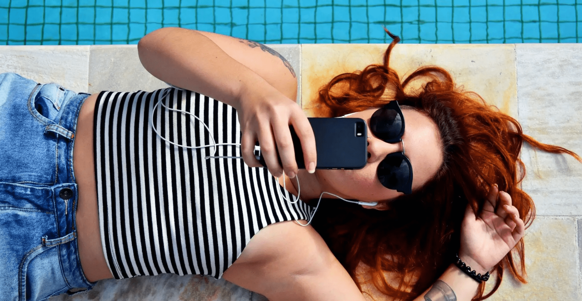 Chica mirando su teléfono junto a una piscina | Unsplash