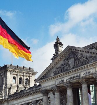 Prompt Deutsch white concrete building with flags on top under blue sky during daytime