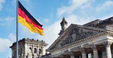 Prompt Deutsch white concrete building with flags on top under blue sky during daytime