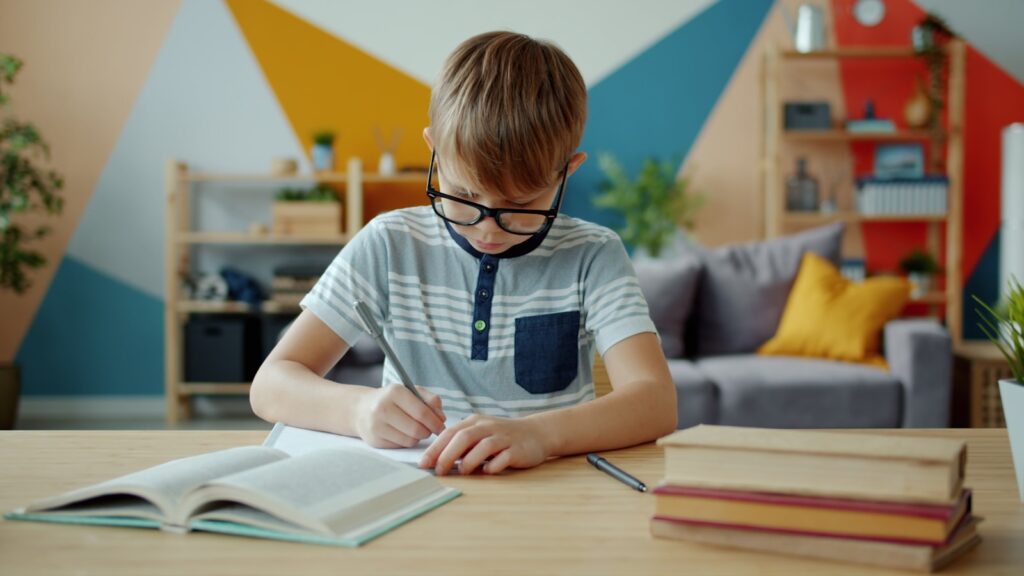niño en escuaela alumno Young boy with glasses writing in a notebook at desk.