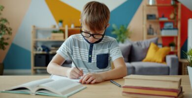 niño en escuaela alumno Young boy with glasses writing in a notebook at desk.