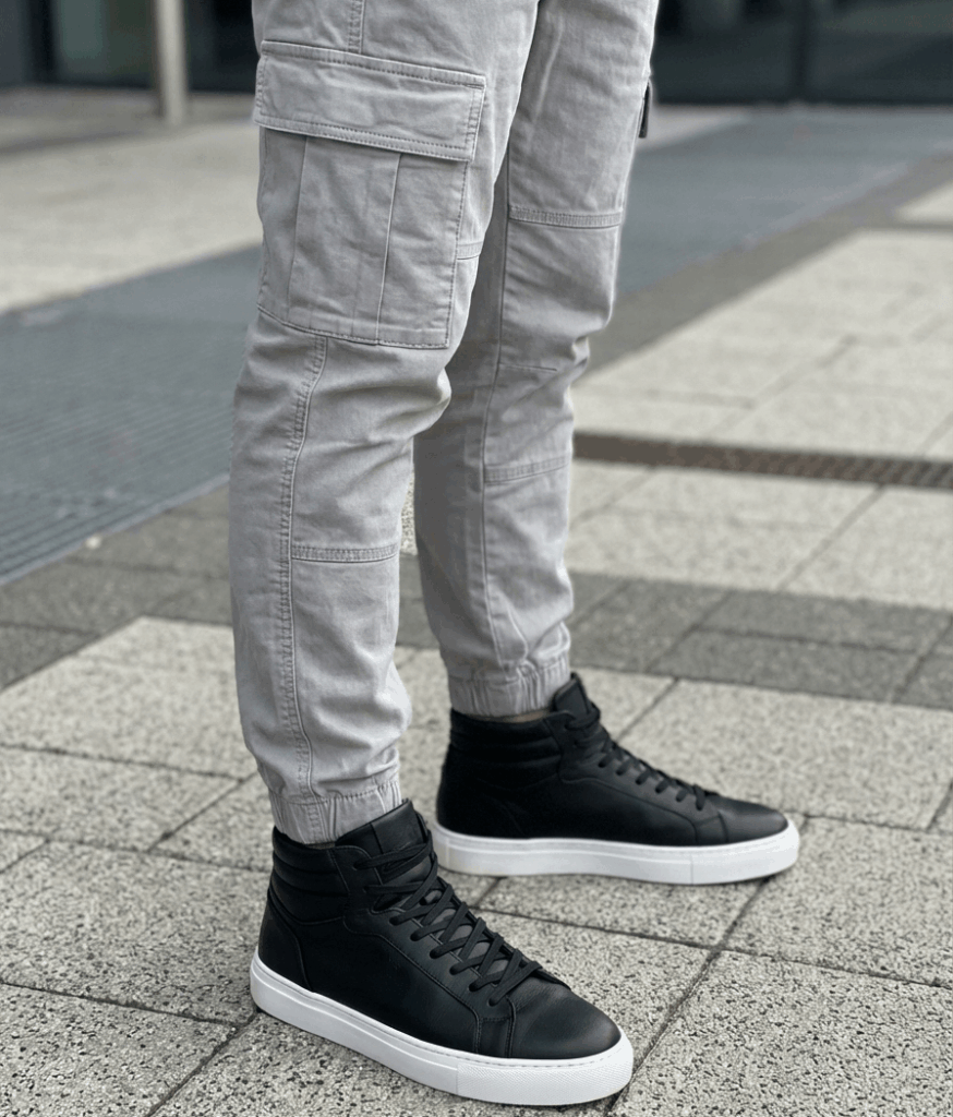 Primer plano de pantalones cargo grises con elástico en el tobillo combinados con zapatillas altas de estilo urbano sobre un fondo neutro